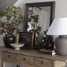 a table with two vases and a lamp on it next to a framed mirror