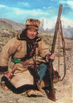 an old photo of a man with a bow and arrow in his hand sitting on the ground