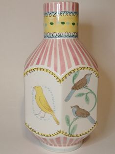 a vase with birds painted on it sitting on a white tableclothed surface next to a pink and yellow striped wall