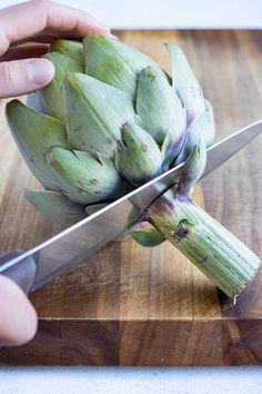 a person cutting up an artichoke on top of a wooden cutting board