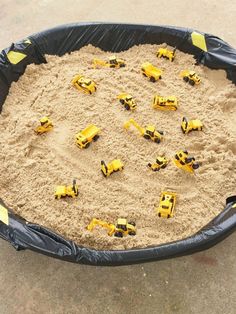 a large black plastic container filled with sand and yellow construction vehicles on top of it