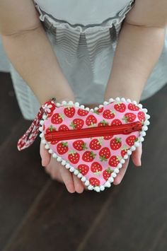 a heart shaped purse with strawberries on it is held by a child's hands