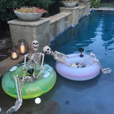 two inflatable skeleton floats sitting next to a pool with an inflatable skeleton floating on it