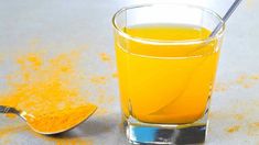 a glass filled with orange juice next to a spoon