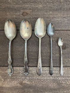 five antique spoons lined up in a row on a wooden surface with one empty