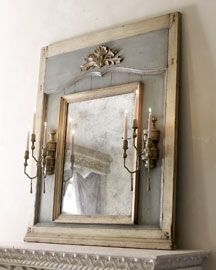 an old mirror is hanging on the wall next to a fireplace mantel with candles