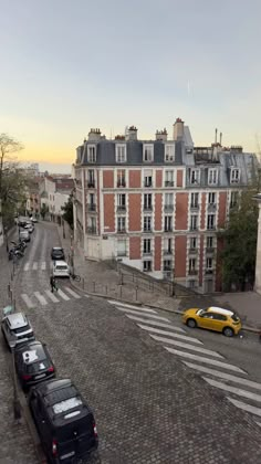 cars parked on the side of a road next to tall buildings and cobblestone streets