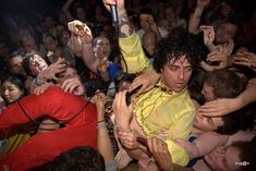 a man in yellow shirt surrounded by people at a music concert with his arms up