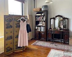 a dress hanging on a clothes rack next to a dresser and mirror in a room with wooden floors