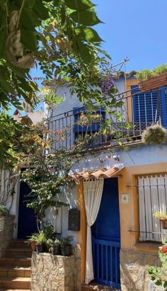 a house with blue doors and shutters on the outside, surrounded by greenery