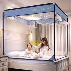 two young women sitting on a bed in a room with white walls and blue canopy