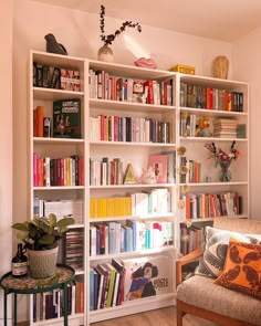 a living room filled with lots of books on top of a white book shelf next to a brown couch