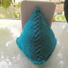 a blue knitted pillow sitting on top of a white table next to a plant