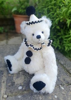 a white teddy bear wearing a black and white hat sitting on the ground next to some plants