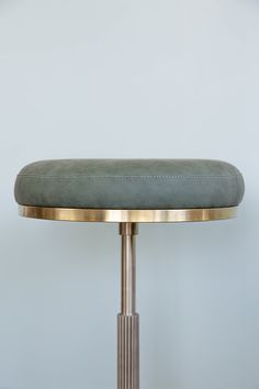 a round metal table with a green cushion on it's top and a white wall in the background