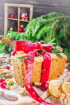 a loaf of bread with red ribbon and decorations around it on a wooden table next to pine cones