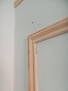 the corner of a white wall with a wooden frame hanging on it's side