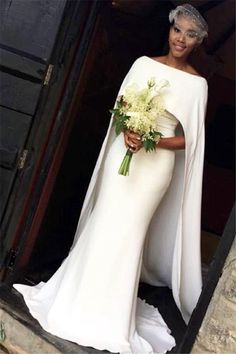 a woman in a white dress and cape holding flowers is standing outside the door to her wedding