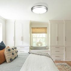 a bedroom with white cabinets and drawers, a bed in the middle is surrounded by pillows