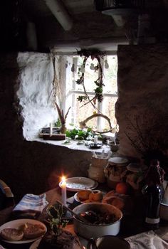 a table filled with food and candles in front of an open window, next to a potted plant