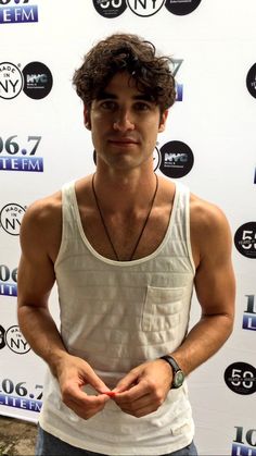 a man standing in front of a white wall with his hands together and looking at the camera