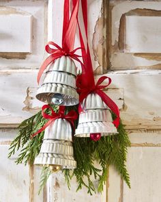 three bells hanging from the side of a door decorated with evergreen and red ribbon bows