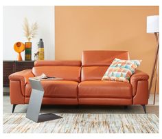 an orange leather couch in a living room next to a table with a laptop on it