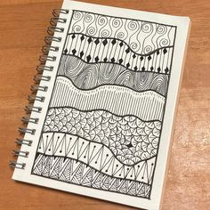 a spiral notebook with an abstract design on the cover, sitting on top of a wooden table