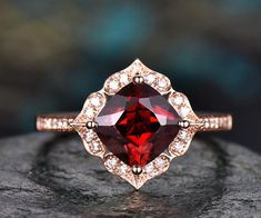 a ring with a large red stone surrounded by small white diamonds on top of a rock