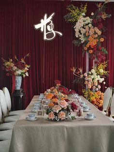 a table with flowers and candles on it in front of a red curtained wall