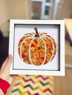 a person holding up a frame with buttons in it and a pumpkin on the inside