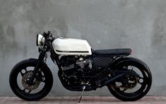 a black and white motorcycle parked in front of a gray wall with no one on it