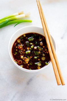 two chopsticks sit next to a bowl of soup with green onions on the side