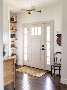 a white front door in a home with wood floors and open shelves on the wall