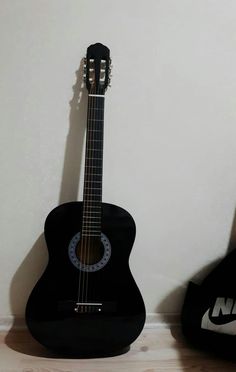 a black acoustic guitar sitting on top of a hard wood floor next to a white wall