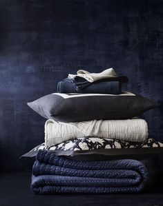 a stack of pillows and blankets sitting on top of each other in front of a black wall