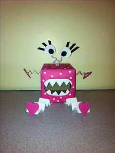 a pink box with googly eyes and hearts on it sitting on a table next to a wall