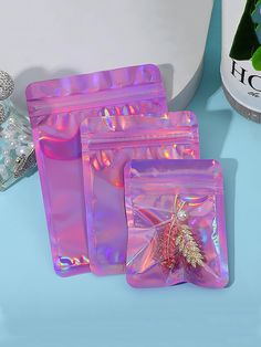 three shiny bags with a small tree in them sitting on a blue table next to a bottle