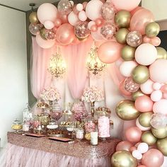 a table topped with lots of pink and gold balloons next to a wall filled with candles