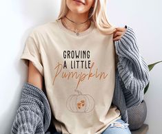 Growing A Little Pumpkin T-Shirt, Fall Maternity Shirt, Pregnancy Thanksgiving Shirt, Funny Pregnancy Shirt, Pregnancy Reveal Shirt "Welcome to our PearlClothingCrafts clothing store! Discover your style, catch the fashion. Enjoy your shopping!" PRODUCTS Tees are Unisex, classic fit. Please refer to size chart in listing photos for details.  FEATURES     *Bella Canvas -unisex size -4.2 oz. -Solid colors are 100% Combed Cotton and Ring-Spun Cotton. -Athletic Heather 90% Combed and Ring-Spun Cotton, 10% Polyester -All Heather CVC Colors 52% Combed and Ring-Spun, 48% Polyester *Gildan SoftStyle -unisex size -Sport Gray : 4.5 oz/yd² | 90% Ring Cotton / 10% Polyester -Heather Navy, Heather Maroon, Heather Galapagos Blue, Dark Heather : 4.5 oz/yd² | 65% Polyester / 35% Ring Cotton -Other Colors Funny Pregnancy Shirts, Shopping Products, Pregnancy Reveal Shirt, Funny Pregnancy, Funny Pumpkins, Fall Maternity, Maternity Shirt, Types Of T Shirts, Pregnancy Humor