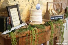 a table topped with a cake covered in green moss next to books and framed pictures