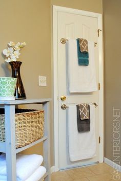 two towels are hanging on the door and in front of it is a basket with flowers