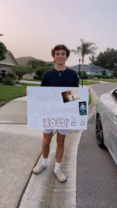 a young man holding up a sign in front of a car on the side walk