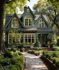 a green house surrounded by lush greenery and lots of trees in the front yard