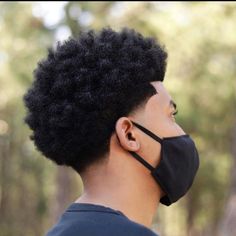 a man wearing a black face mask with an afro haircut on his head in the woods