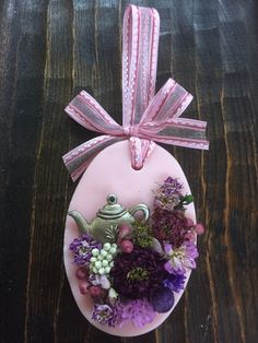 a ceramic teapot with purple flowers and a pink ribbon tied around it on a wooden table