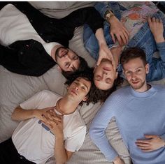 four people are laying on the bed with their arms around each other and looking at the camera