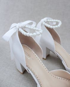 a pair of white high heel shoes with pearls on the toe and heels are tied together