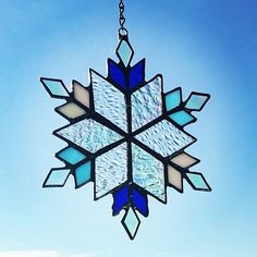 a stained glass snowflake hanging from a chain on a blue sky background with clouds