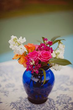 a blue vase filled with colorful flowers on top of a white and blue table cloth